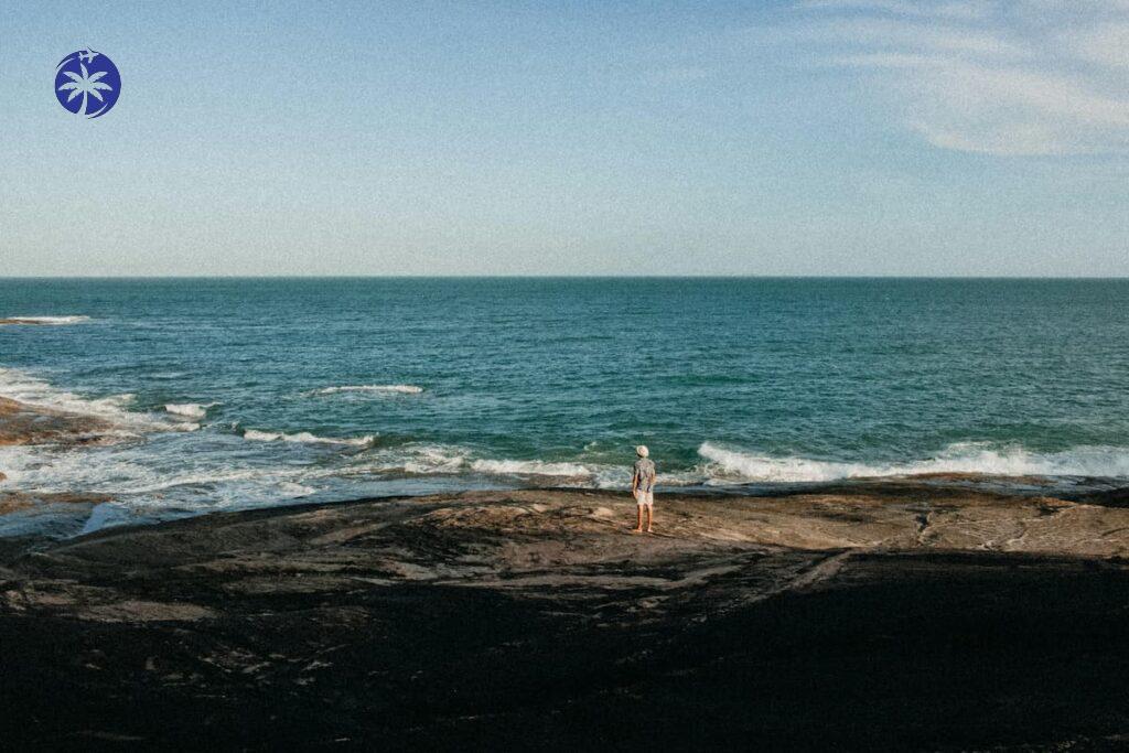 Imagem mostra homem relaxando à beira da praia.